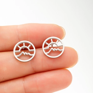 Close-up of circular cutout earrings with sun and mountain pattern held in fingers