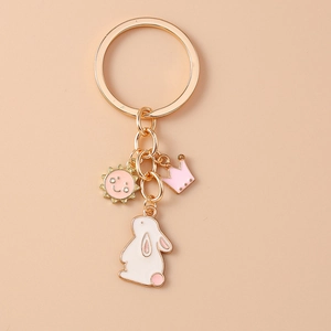 Detail of golden metal keychain featuring pink rabbit, smiling sun, and crown charms