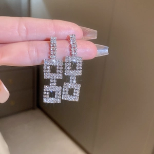 Close-up of luxury silver drop earrings with sparkling square crystals held by hand