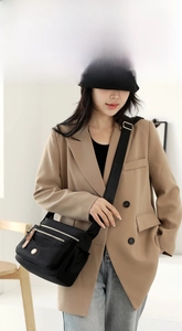 Close-up of black nylon crossbody bag with gold zippers on a stylish model in a beige suit