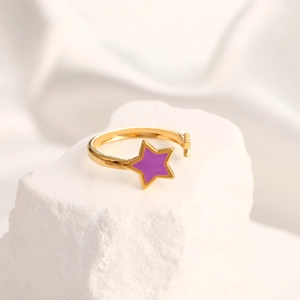 Detail of a golden open ring with a purple star enamel inlay on a textured stone surface
