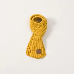Close-up of yellow knitted kids scarf featuring rib-knit texture and brown leather patch