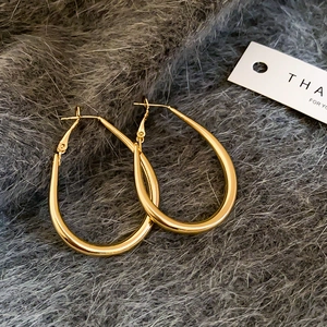 Detailed view of polished gold U-shape oval hoop earrings on dark grey faux fur background