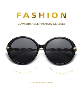 Close-up of black oversized sunglasses with decorative gold leaf metal hinges and wavy arms
