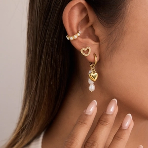 Detail of 18K gold earrings with pearls, heart charms, and zircon studs on model ear