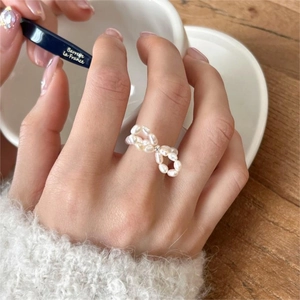 Detail of a handmade Baroque pearl bow ring with silver bead on a woman finger