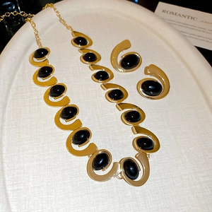 Detail of gold oval necklace and earring set featuring black gemstones on a tray