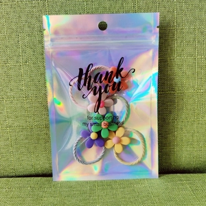 Holographic zip bag with 'thank you' text containing five colorful flower hair ties