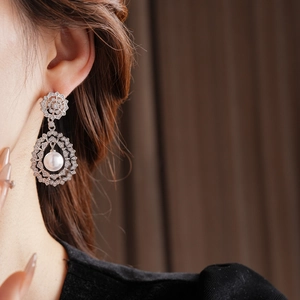 Detail of vintage teardrop pearl earring with flower stud and zircon inlays on model