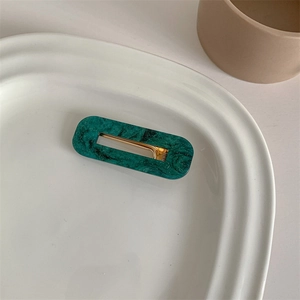 Detailed macro view of green marble pattern acetate hair clip on a white ceramic tray