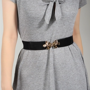 Women's black elastic waist belt with gold bow buckle styled on a gray dress