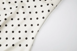 Detailed view of white woven fabric with black polka dot print and precise stitching line