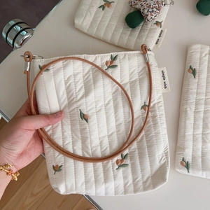 Detail of quilted crossbody bag with orange berry embroidery and brown braided strap