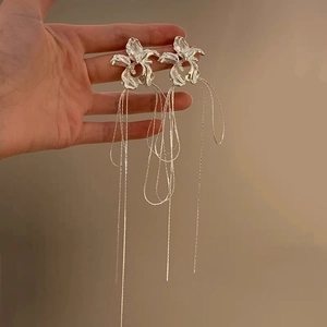 Detail of silver floral drop earrings with long tassel chains held by hand