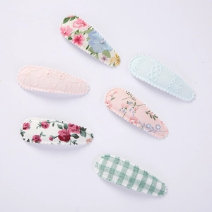 Detail of six fabric hair clips with floral, lace, and plaid patterns on white background