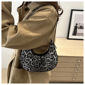 Side view of leopard print crescent bag with thin strap on a beige coat model