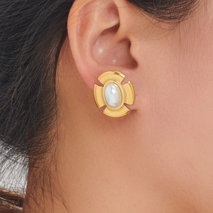 Close-up of vintage gold cross earrings with oval pearls on model ear lobe