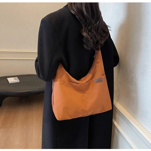 Detail of a large orange canvas tote bag with a fashion label worn on a black coat