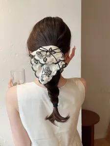 Detail of a beige lace hair scrunchie with black rose pattern, ribbon bow and pearl bead