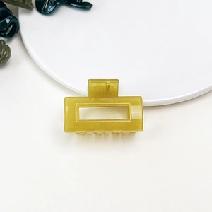 Macro detail of glossy yellow rectangle hair claw clip on white ceramic surface