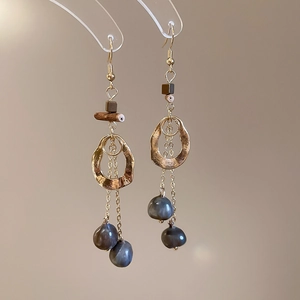 Macro view of gold hammered hoops with wood beads and baroque pearl tassel earrings