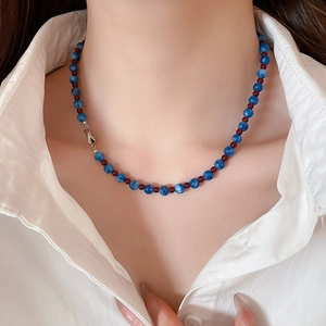Close-up of blue beaded necklace with red accents on a model wearing a white shirt