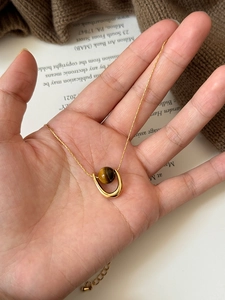 Detail of U-shape pendant necklace with tiger eye stone held in hand for size visualization