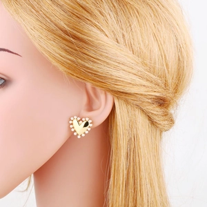 Elegant gold heart earrings with white pearls around the edge worn on a model's ear