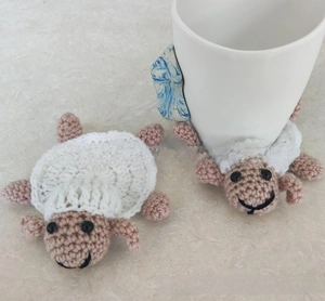 Handmade crochet sheep coasters holding a white ceramic mug on a marble table