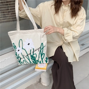 Close-up of a white floral canvas tote bag showing the green plant print and shoulder straps