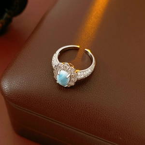 Macro detail of silver ring with blue oval gemstone and zircon accents on leather box