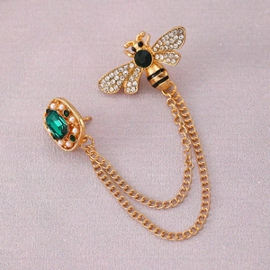 Macro detail of bee chain brooch with emerald gemstone and pearl accents on fabric