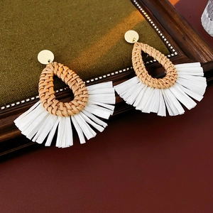 Detailed shot of raffia water-drop earrings with white tassels on a vintage wooden frame