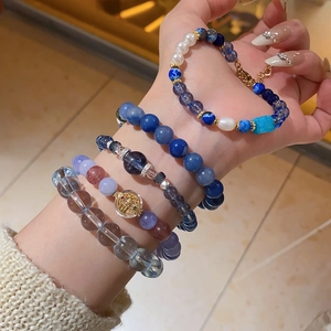 Close-up of layered beaded bracelets with blue lapis, quartz and gold coin charms