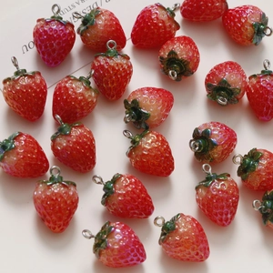 Detailed view of red resin strawberry charms with silver hooks for DIY jewelry making