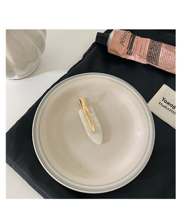 Detailed close-up of a white marble acetate hair clip on a ceramic tray in a soft setting