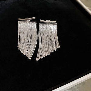 Detailed view of silver tassel drop earrings with sleek metal chains on black velvet background