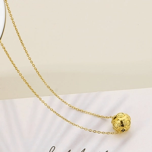 Close-up of golden stainless steel necklace with textured concentric circle ball pendant