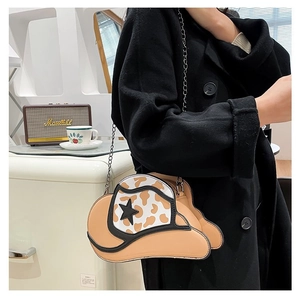 Detail shot of a cow print cowboy hat shaped crossbody bag with a metal chain strap