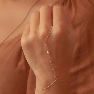 Close-up of gold finger bracelet featuring white zircon stones and small round beads on hand