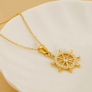 Elegant gold rudder necklace with white zircon stones on a white ceramic dish