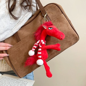 Detailed view of red plush pony charm with striped scarf on a brown suede bag