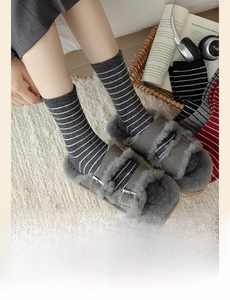 Detail of grey striped wool socks paired with cozy faux fur buckle slippers on a rug