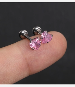 Détail de petites boucles d'oreilles cœur rose sur le bout des doigts pour l'échelle