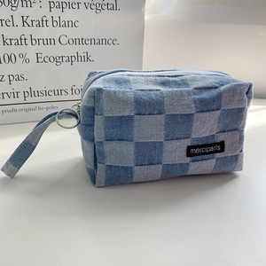 Detalle de estuche de lona a cuadros azules con cremallera redonda y asa tejida