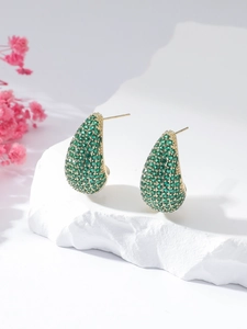 Close-up of gold teardrop earrings with pavé green gemstones on stone stand