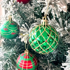 Close-up of decorative Christmas ornaments with red and green patterns on a snowy tree