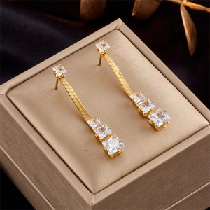 Golden snake chain earrings with square green crystals displayed on a luxury jewelry box