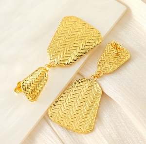 Close-up of gold-plated geometric earrings with intricate woven texture on stone tray