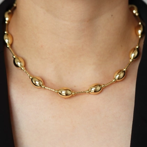 Close-up of 18k gold plated oval beads necklace worn on neck with polished metal finish